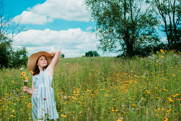 Teen girl standing on grassy field against yellow flowers