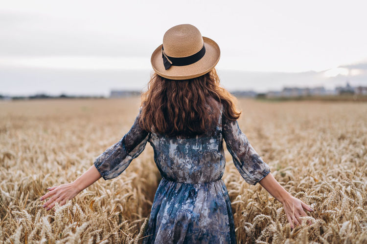 Rear view of woman wearing hat standing amidst crops in farm