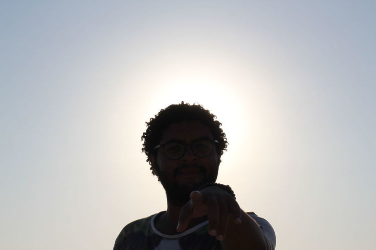 Low angle view of young man pointing against clear sky during sunset