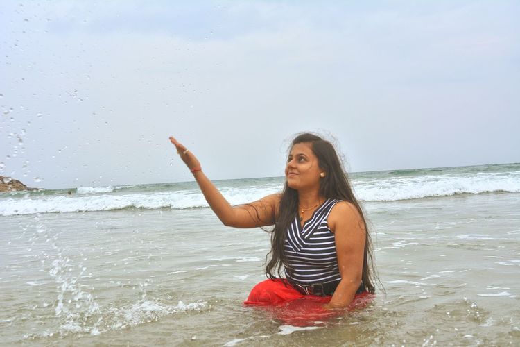 Young woman gesturing while looking up in sea against sky