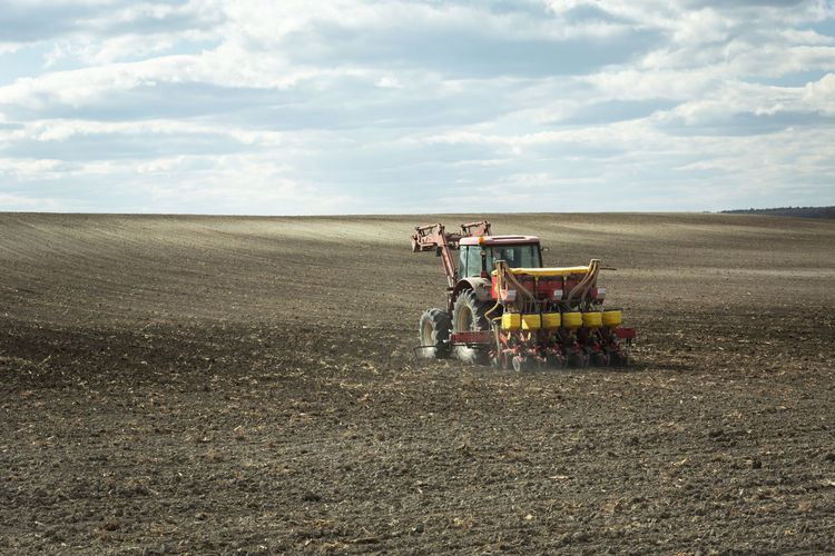 Tractor fertilizing the plowed field, clouds and sky