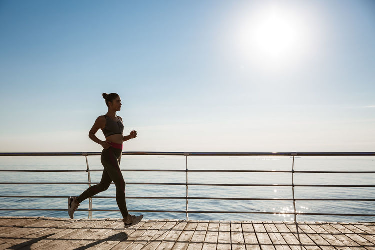 Woman jogging by sea against clear sky