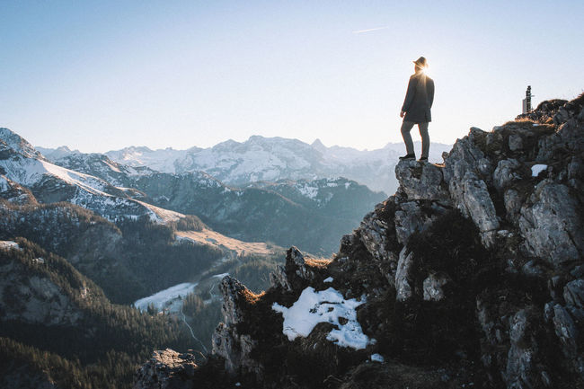 Low angle view of man standing on rocky mountains against clear sky during sunny day