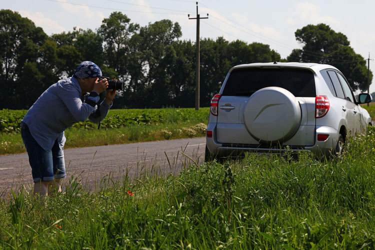 Man photographing by grassy field on road