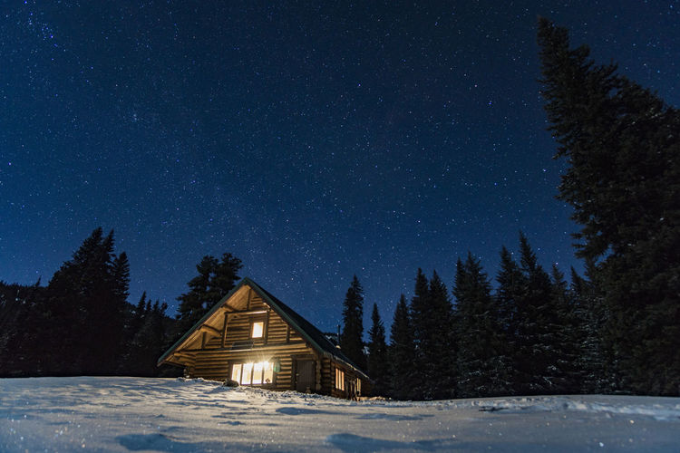 Illuminated house on snowcapped landscape against star field sky