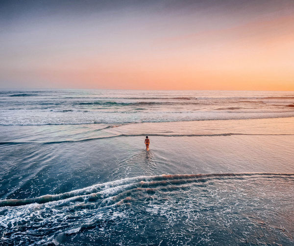 Woman wading in sea against sky during sunset