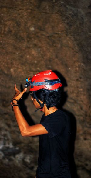 Side view of young man wearing helmet standing against rock formation in cave