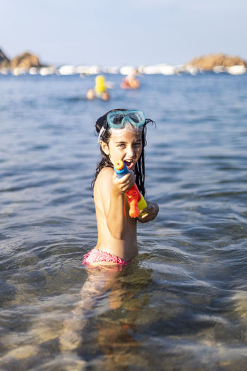 Portrait of girl playing with squirt gun while standing in sea