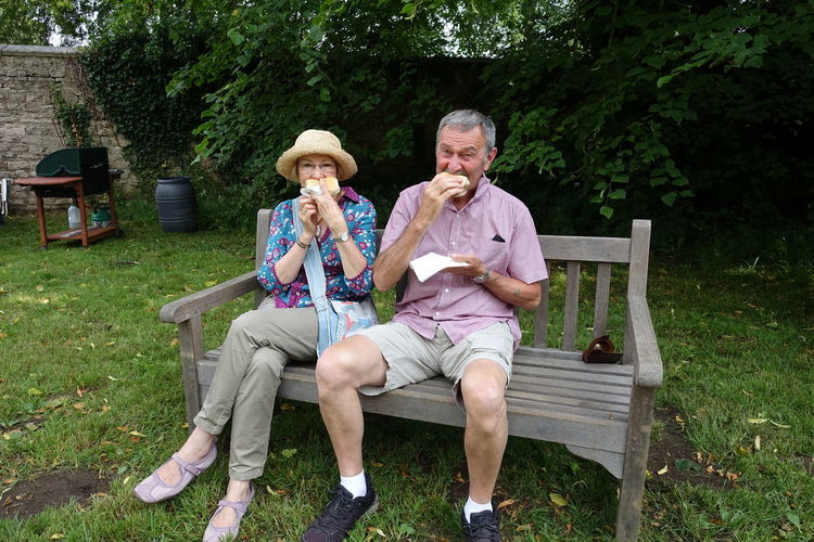 Portrait of couple eating food while sitting on bench in park
