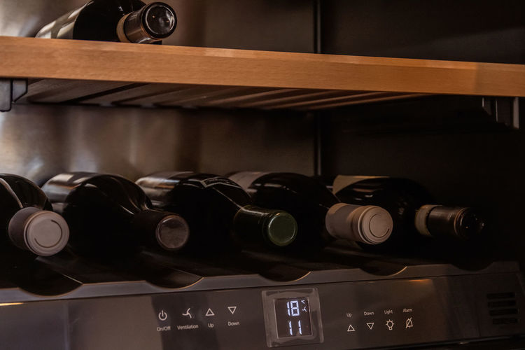 Bottles of assorted wine placed on shelf in contemporary cabinet with humidity control placed in kitchen of apartment
