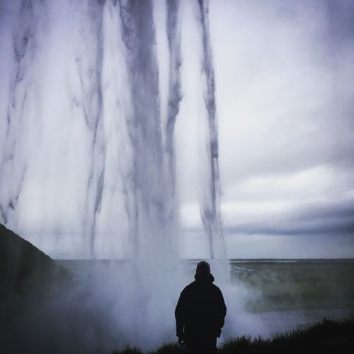 Rear view of silhouette man standing against waterfall