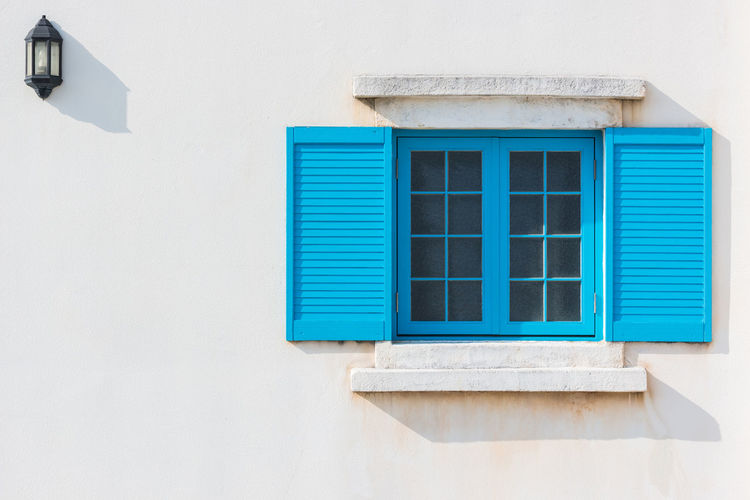 Colorful blue window and detail of house exterior on white wall.