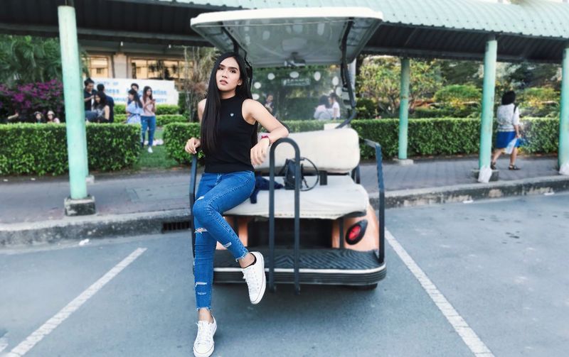 Portrait of young woman sitting on golf cart in city