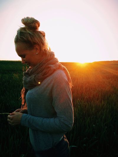 Side view of young woman standing on field at sunset