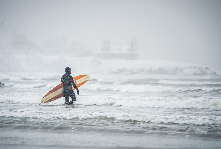 Surfer walking out to waves during a snow storm in maine