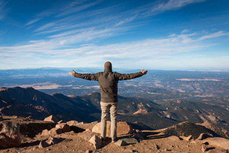 Rear view of man standing on top of pikes peak, colorado with arms wide open against sky
