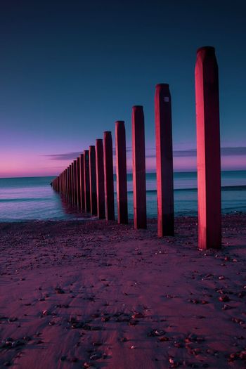 Row of wooden posts at beach against sky