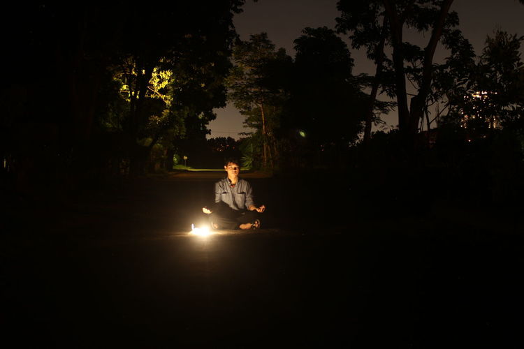 Man sitting in illuminated park against sky at night