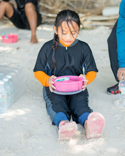 Girl holding lunch box while sitting on land at beach