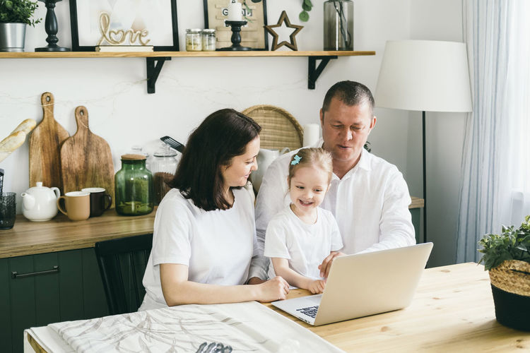 Cheerful family sits in the kitchen takes a laptop screen.