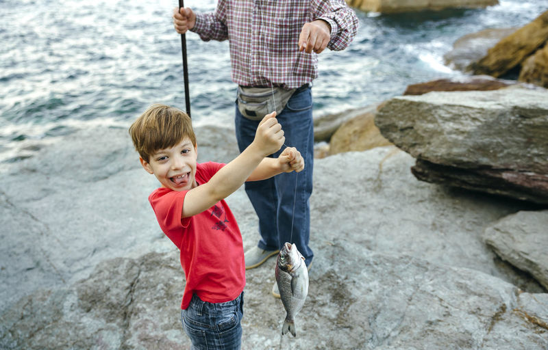 Happy boy holding fish on fishing line caught by his grandfather