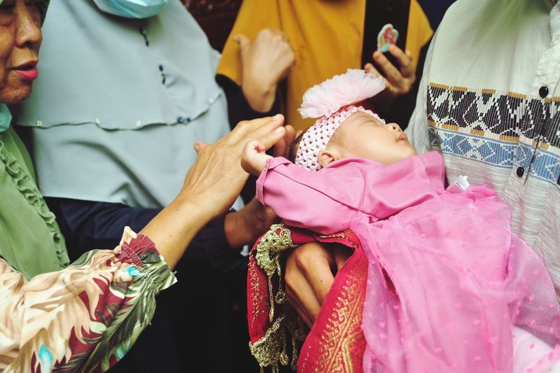 A child is caressed by his grandmother while sleeping on his father's lap on aqiqah event