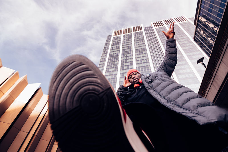 Hip hop man walking above the camera lens under skyscrapers - stylish african american dj 