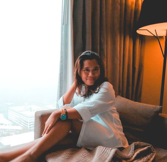 Portrait of woman sitting on sofa by window at hotel