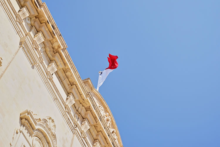 Waving maltese flag on parliament building against blue sky low angle view with copy space