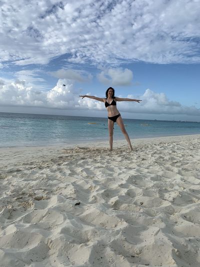 Full length of woman wearing bikini while standing at beach against sky