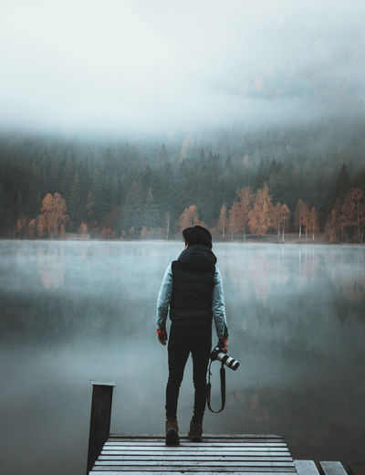 Rear view of man standing on jetty by lake during foggy weather