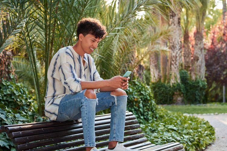 A young man with afro hair watching his smartphone sitting on a bench