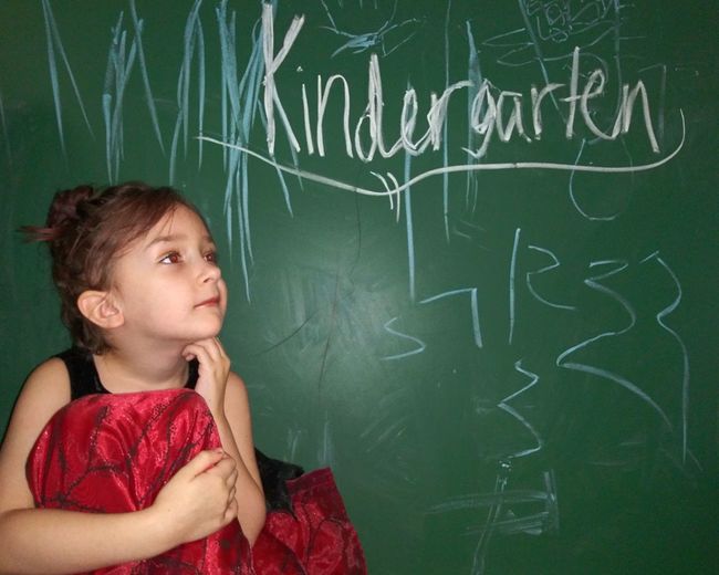 Cute girl looking away against kindergarten text on blackboard