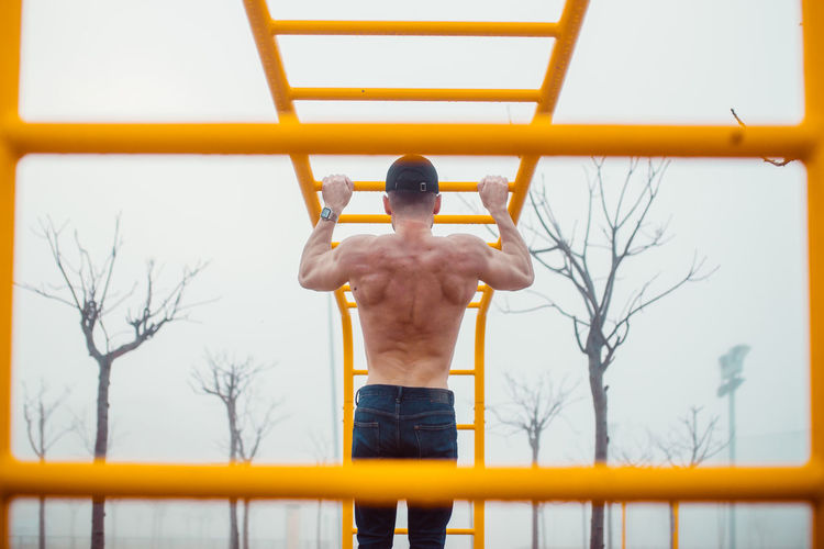 Rear view of shirtless man standing on wall