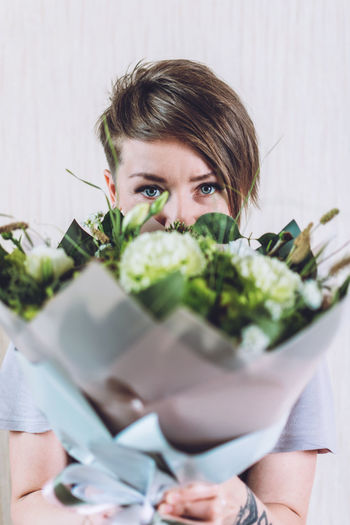 Portrait of woman holding bouquet against wall