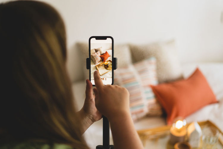 A young woman is filming home goods for her online store on her phone camera.