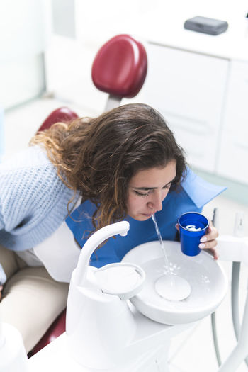 Woman spitting water in sink at dental clinic