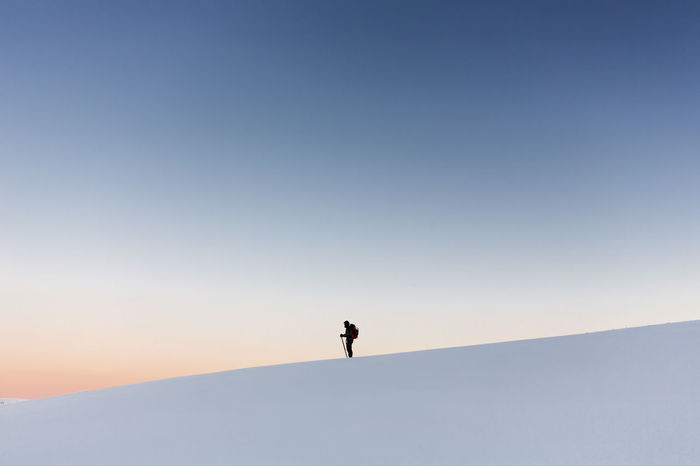 Man standing on snowcapped mountain against clear sky at sunset