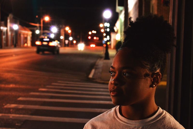 Teenage girl looking away on road in city at night