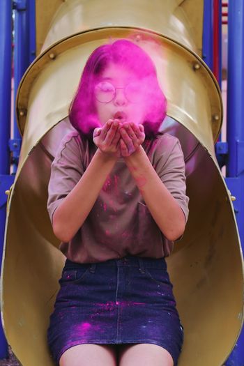 Girl blowing face powder while sitting on tube slide at playground