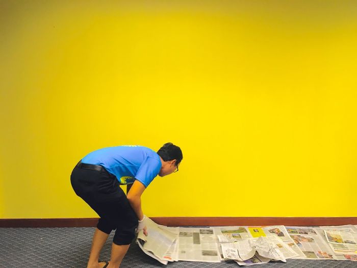 Side view of man standing against yellow wall