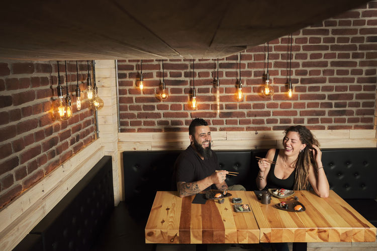 Loving couple eating appetizing sushi while sitting at wooden table in japanese restaurant