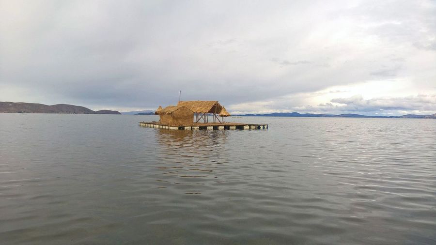 Thatched hut on floating platform in lake titicaca against cloudy sky