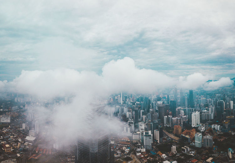High angle view of modern buildings in city against sky under low clouds 