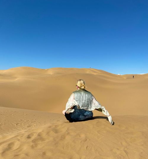 Rear view of woman with scarf on desert against clear sky