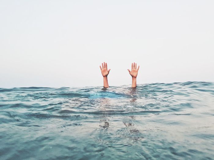 Cropped hands of person emerging from sea against clear sky
