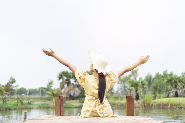 Rear view of woman sitting by lake against sky