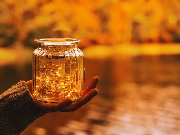 Cropped hand of woman holding string light in jar against lake