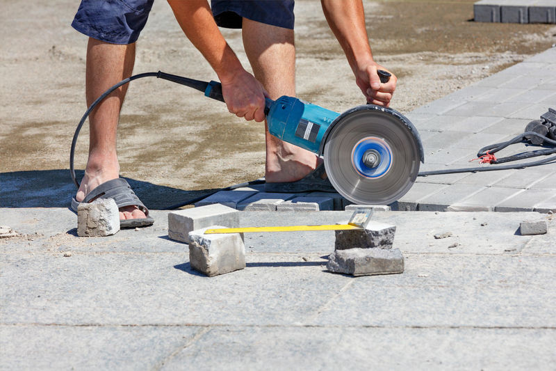 A builder holds a working electric saw with a diamond blade and cuts a curb. 