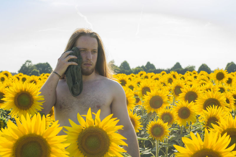 Thoughtful shirtless man wiping himself from towel while standing amidst sunflowers